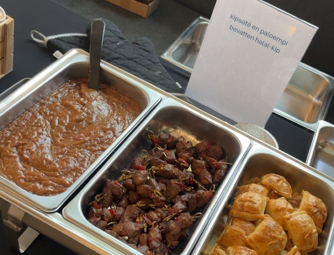 Chafing dishes met pindasaus, kipsaté en mini-Paloempies, met een bordje ernaast waarop staat dat de kipsaté en paloempi halal-kip bevatten