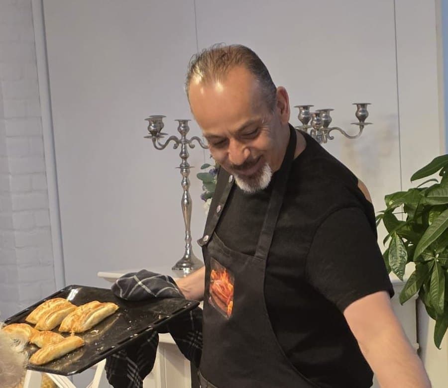 Dennis loopt langs de tafel met een bakplaat vers gebakken Paloempies, in schort met het logo van Paloempie Factory