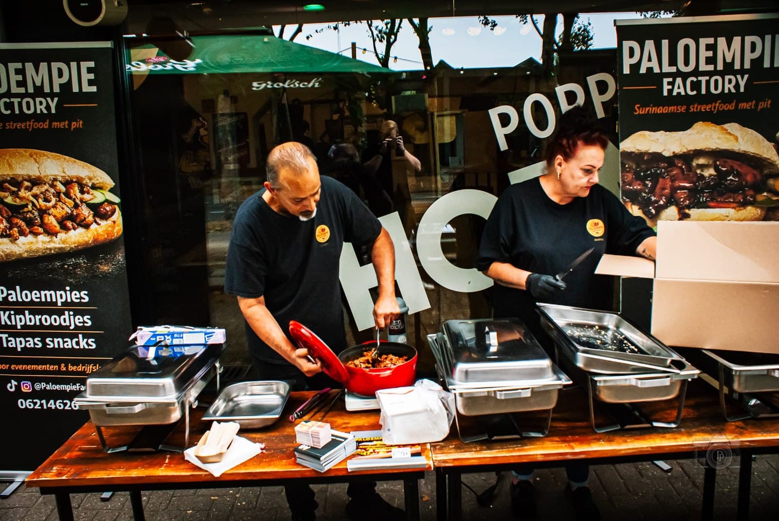 Dennis en zijn partner achter een kraam op straat, met chafing dishes en twee banners van Paloempie Factory