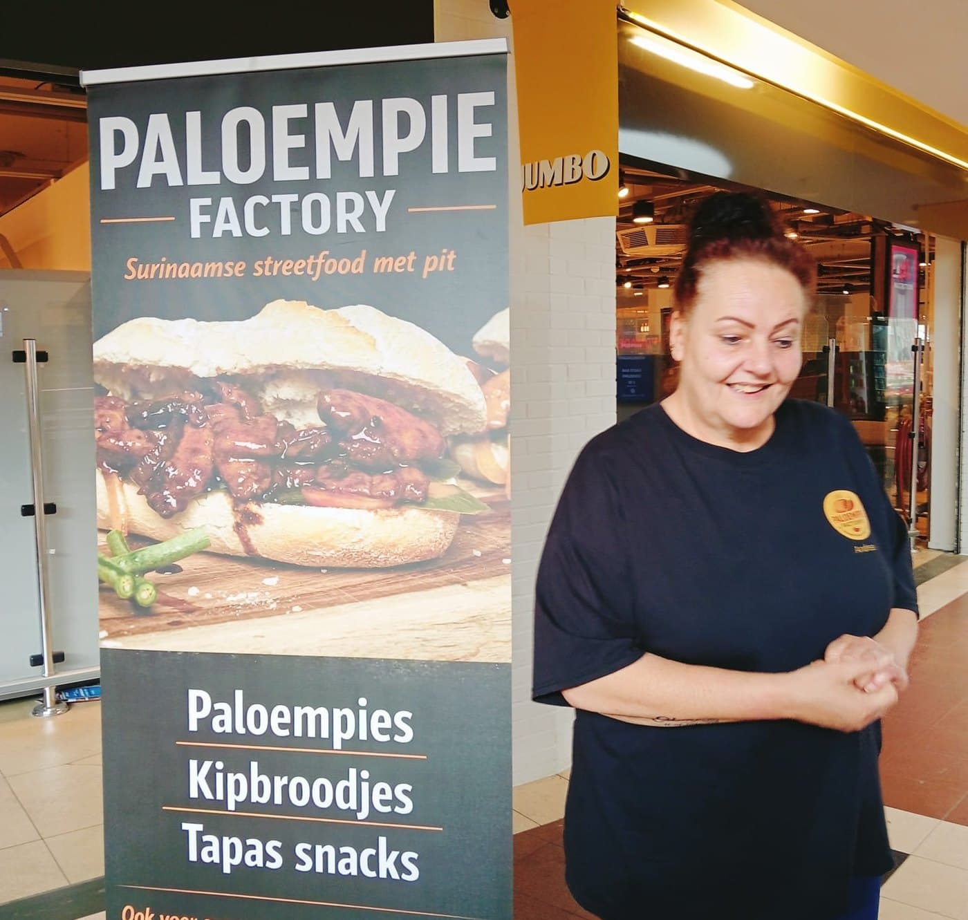 Een banner van Paloempie Factory bij de ingang van een winkelcentrum, met ernaast iemand van het team