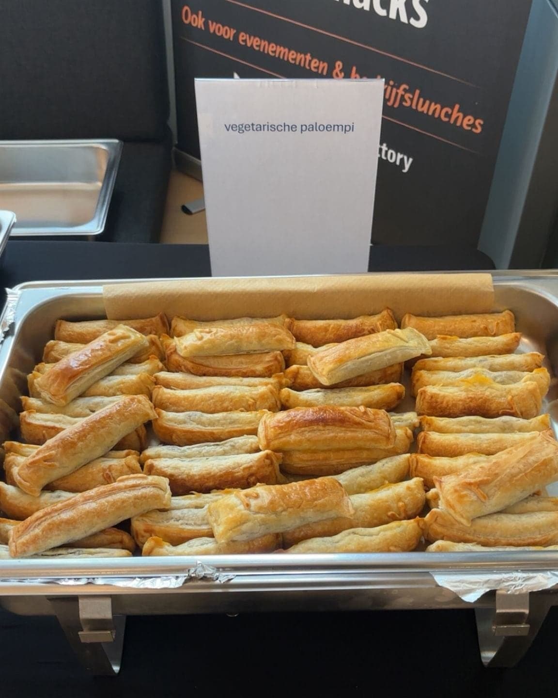 Een volle bak vegetarische Paloempies warm op locatie, met een bordje erbij en de banner erachter waarop staat: ook voor evenementen en bedrijfslunches