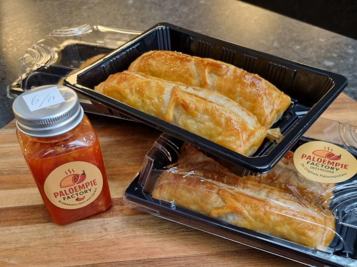 Twee bakjes met verpakte Paloempies op een houten plank, met een fles Paloempiesaus ernaast